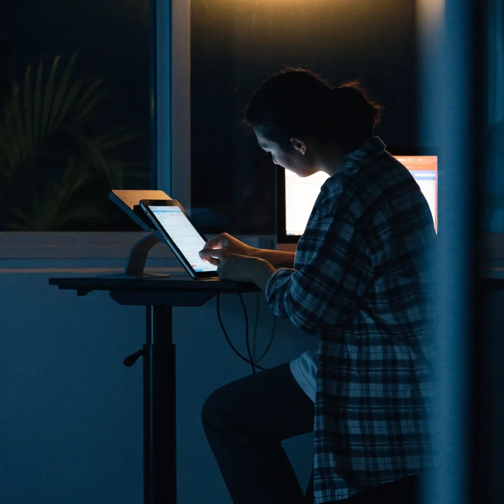 Two hands working at a laptop and an angled monitor in a dark studio, screen glow out of focus